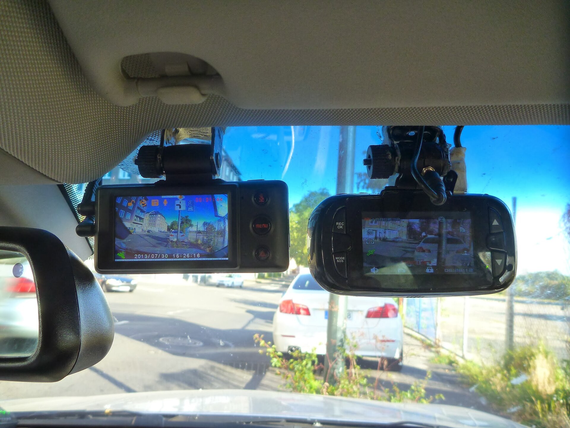 Two dashcams mounted on a windscreen behind the rear-view mirror, both showing a live picture