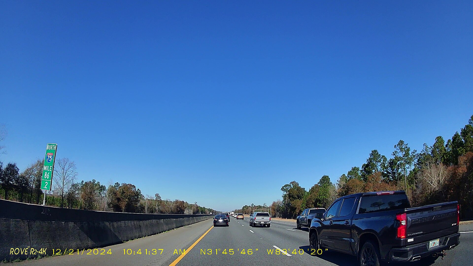Dashcam view of a sunny four-lane interstate with a mile marker and a pickup truck alongside